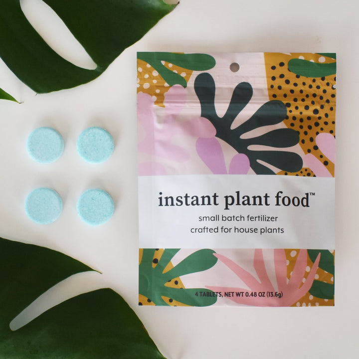 Four light blue fertilizer tablets next to a pouch of Instant Plant Food houseplant fertilizer.